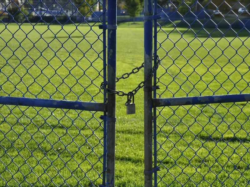Chain link fence with a padlocked double walk gate in front of a wide green field