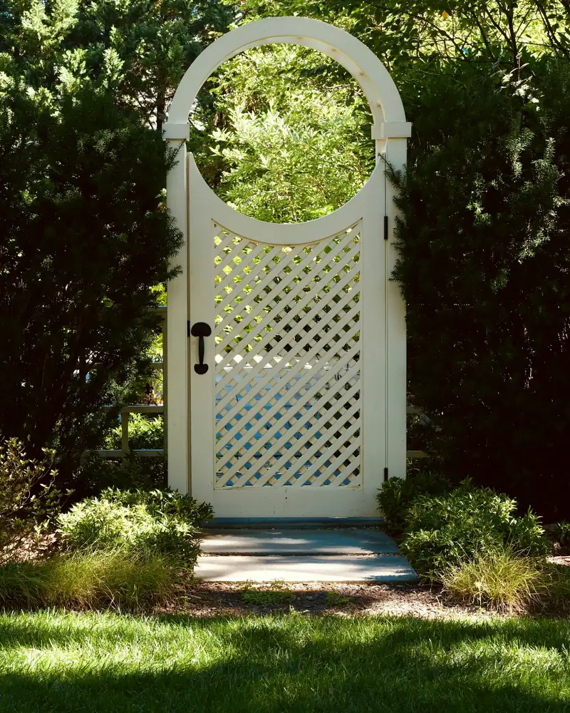 White lattice walk gate with an arched top set into a hedge