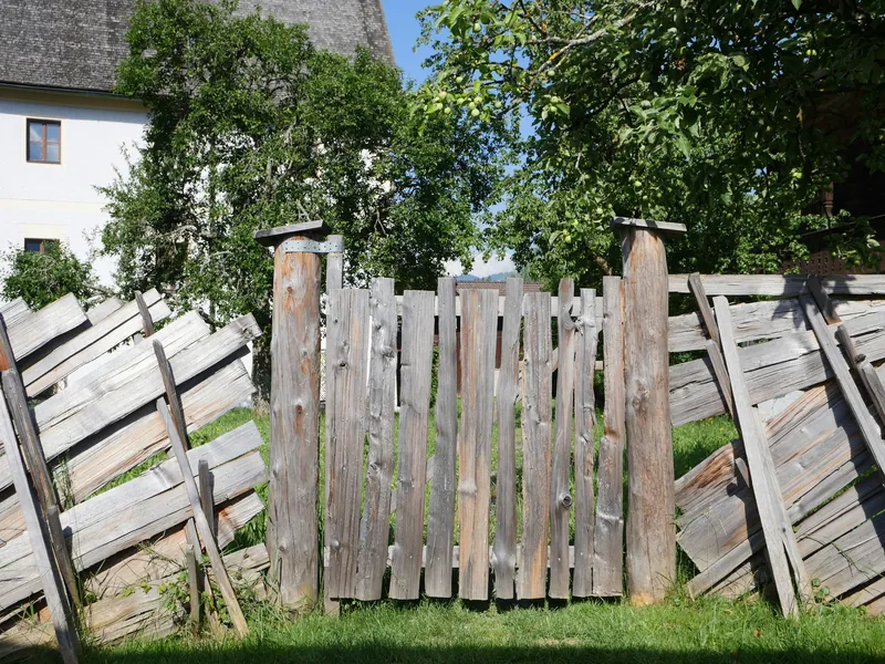 Old wood privacy fence with panels leaning and falling over beside a newer section, the kind of damage a storm leaves
