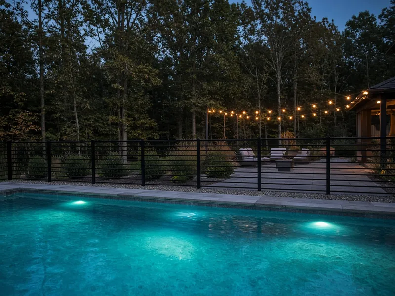 Black horizontal-rail pool fence with lit pool at dusk