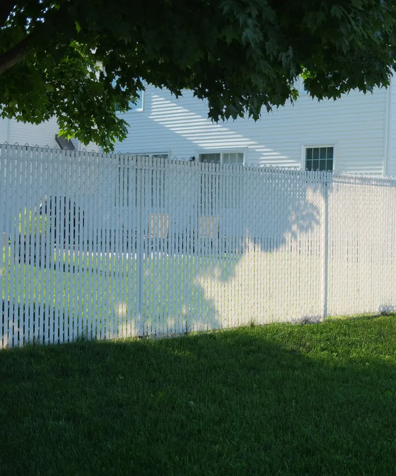 White vinyl privacy fence along the side of a green lawn beside a two-story house
