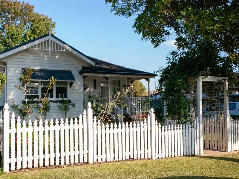 White wood picket fence with a matching arbor gate in front of a porch house and green lawn