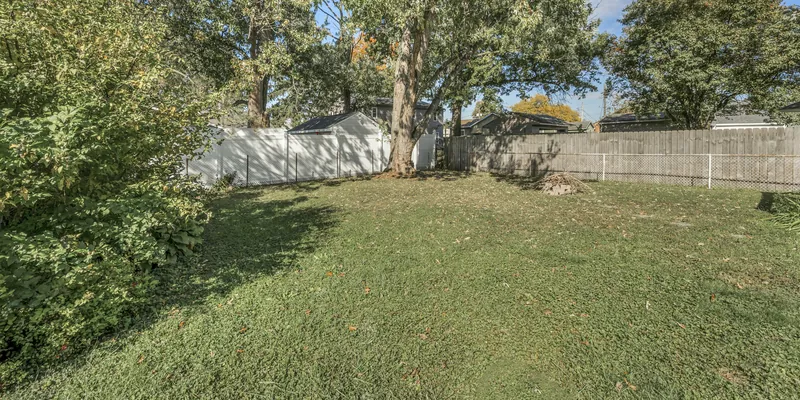Mowed backyard under a big shade tree, closed in by white vinyl and wood privacy fencing